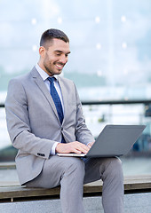 Image showing smiling businessman working with laptop outdoors