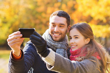 Image showing smiling couple with smartphone in autumn park