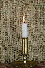 Image showing Single candle in candlestick at burlap background