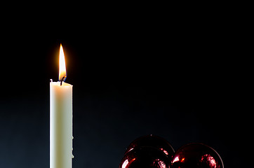 Image showing A burning candle with red christmas balls