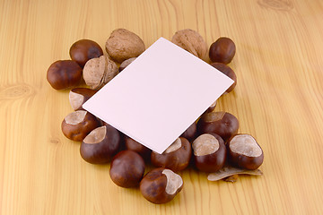 Image showing autumn chestnuts on wooden background and blank paper card