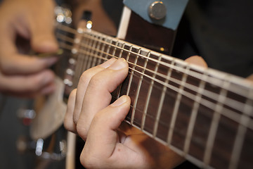 Image showing close up shot of a man with his fingers on the frets of a guitar