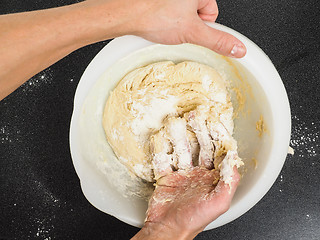 Image showing Person kneading a sticky dough in white bowl on black table