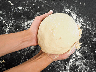 Image showing Person holding a proven dough over black table with flour mess