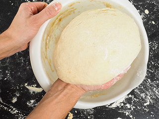 Image showing Person lifting a proven dough out from a white plastic bowl on b