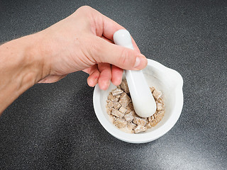 Image showing Person crushing brown sugar cubes in a white marble mortar on bl