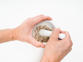 Image showing Person crushing brown sugar cubes in a white marble mortar