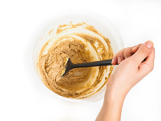 Image showing Person stirring a bake mix in white plastic bowl with black spatul