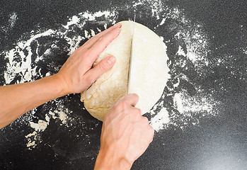 Image showing Person cutting a dough into two pieces on a black table with flo