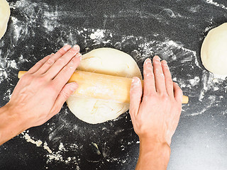 Image showing Person handling a dough with a rolling pin floured black table