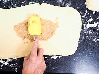 Image showing Person spreading cinnamon mix with spatula onto a flattened doug