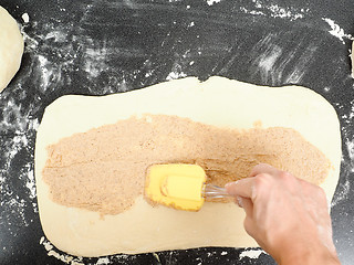 Image showing Person spreading cinnamon mix with spatula onto a flattened doug