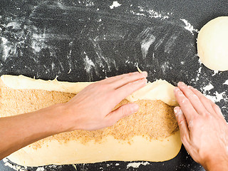 Image showing Person rolling a snail bun with sugar and cinnamon spread