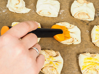 Image showing Person glazing plaited baked goods with egg wash