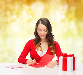 Image showing smiling woman with gift box writing letter