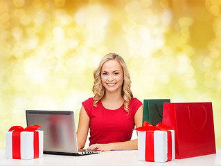 Image showing smiling woman in red shirt with gifts and laptop