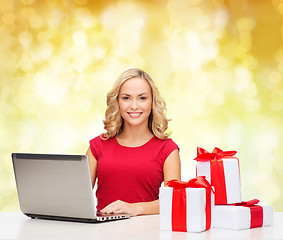 Image showing smiling woman in red shirt with gifts and laptop