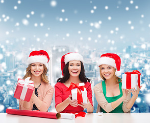 Image showing smiling women in santa helper hats packing gifts