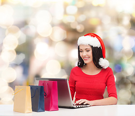 Image showing smiling woman in santa hat with bags and laptop