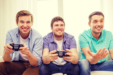 Image showing smiling friends playing video games at home