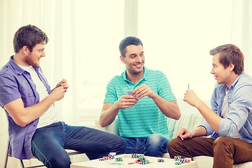 Image showing happy three male friends playing poker at home