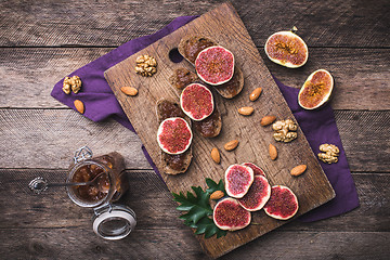 Image showing Sliced figs, nuts and bread with jam on choppingboard in rustic 