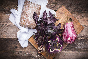 Image showing Aubergines, basil and bread on chopping board and wood