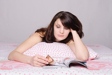 Image showing Beautiful girl thoughtfully reading a magazine in bed