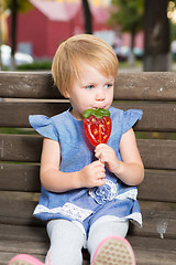 Image showing Beautiful little girl holding strawberry shaped lollipop