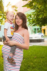 Image showing Laughing young pregnant mother playing with her son in a beautiful garden