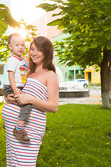 Image showing Laughing young pregnant mother playing with her son in a beautiful garden