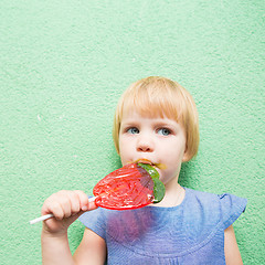 Image showing Beautiful little girl holding strawberry shaped lollipop