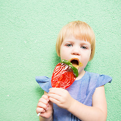 Image showing Beautiful little girl holding strawberry shaped lollipop