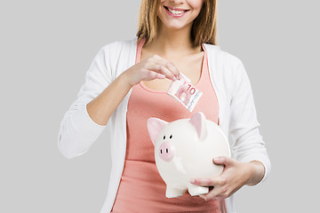 Image showing Beautiful woman putting money in a piggy bank