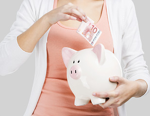 Image showing Beautiful woman putting money in a piggy bank