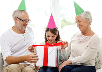 Image showing smiling family in party hats with gift box at home