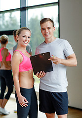 Image showing smiling young woman with personal trainer in gym