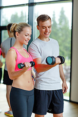 Image showing smiling young woman with personal trainer in gym