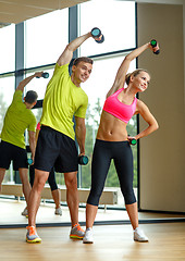 Image showing smiling man and woman with dumbbells in gym