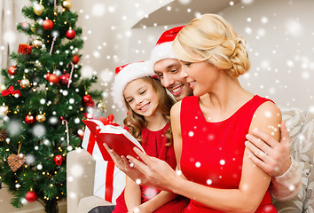 Image showing smiling family in santa hats reading book at home