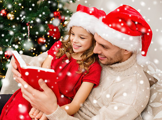 Image showing smiling father and girl in santa hats reading book