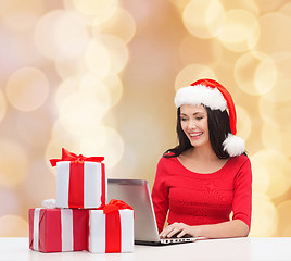 Image showing smiling woman in santa hat with gifts and laptop