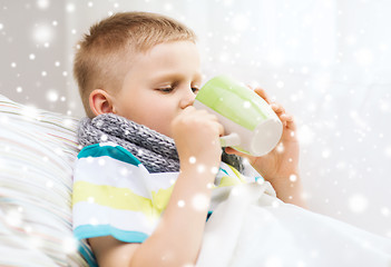 Image showing ill boy with flu in bed drinking from cup at home