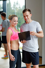 Image showing smiling young woman with personal trainer in gym