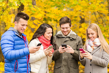 Image showing smiling friends with smartphones in city park