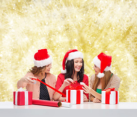 Image showing smiling women in santa helper hats packing gifts