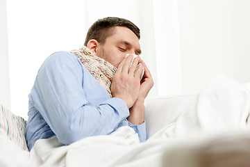 Image showing ill man in scarf blowing nose at home