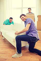 Image showing smiling friends with sofa and boxes at new home