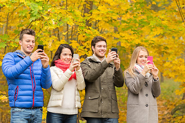 Image showing smiling friends with smartphones in city park