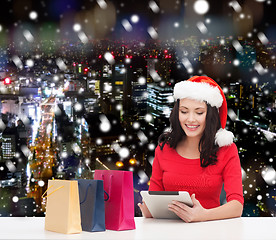 Image showing smiling woman in santa hat with bags and tablet pc